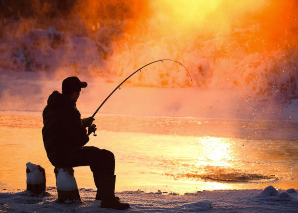 Man ice fishing at sunset
