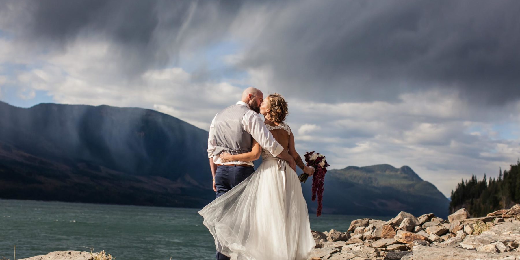 Newlyweds kissing in front of Arrow Lake